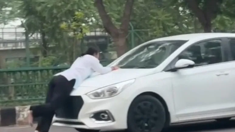 Barefeet, she is pedalling backwards, with her body bent at the middle, covering the car's
